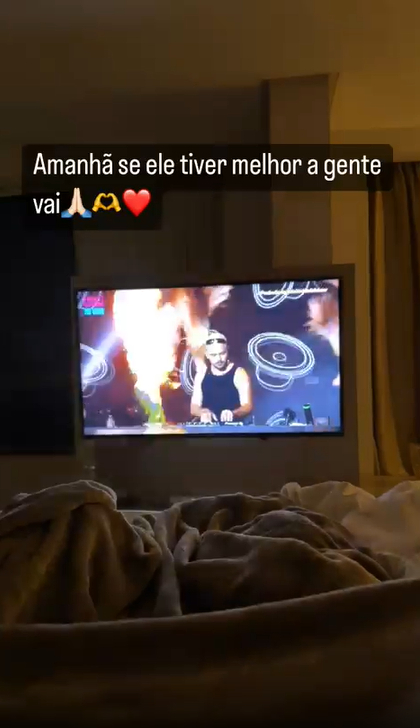 Carlinhos Maia exibe vídeo de uma televisão enquanto está deitado ao lado de Lucas Guimarães, que dorme. NA TV, um DJ toca. Na legenda do vídeo, ele diz que irá ao evento de Gkay se o ex-marido melhorar