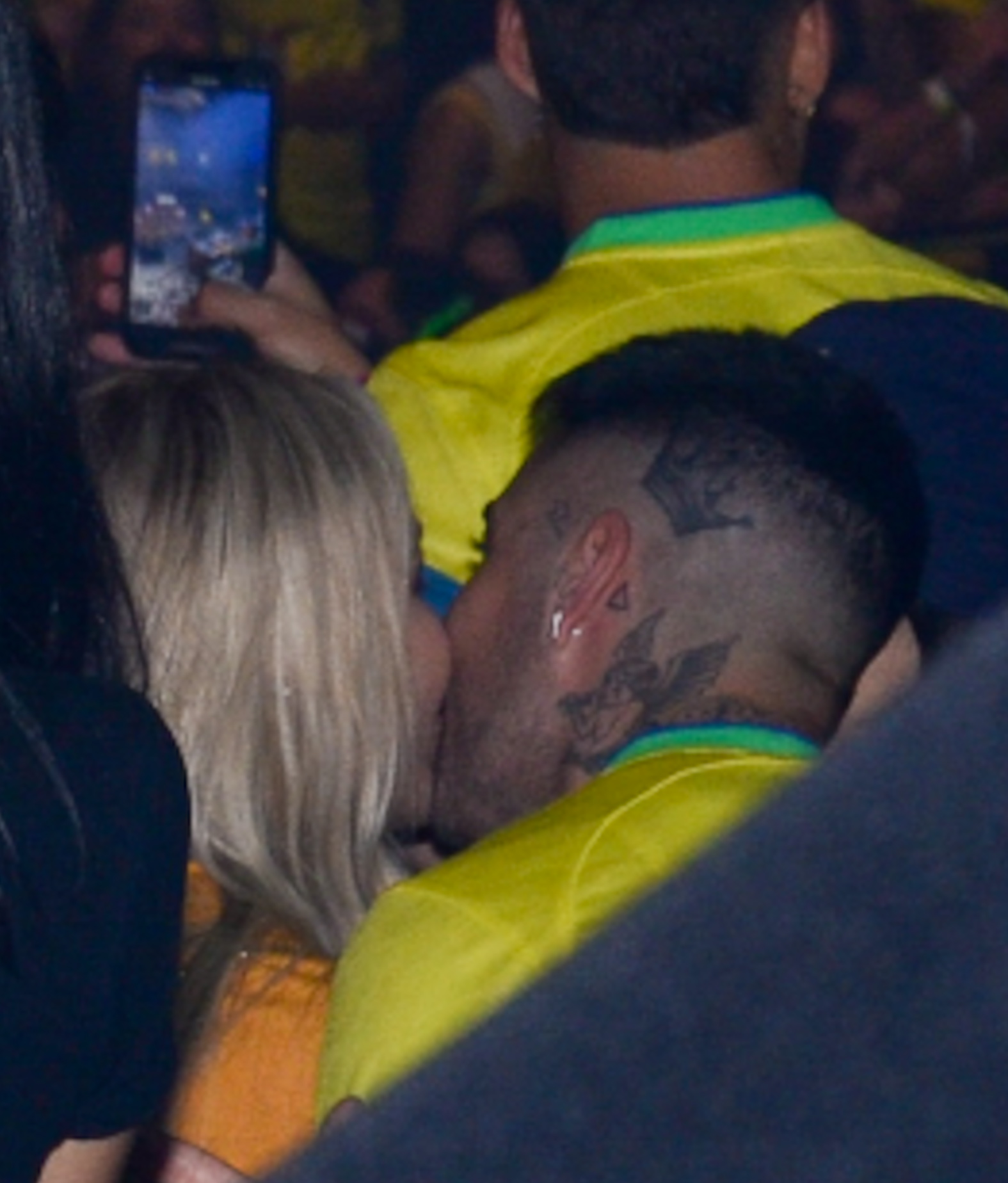 Gui Araújo e Karoline Lima sorridente equanto trocam um beijo no cantinho da boca. Ambos aparecem com camisas amarelas da seleção brasileira