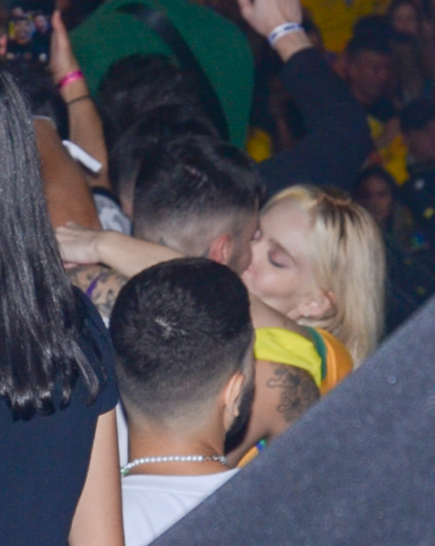 Karoline Lima aparece dando um beijão em Gui Araújo, ela usa uma camisa amarela do Brasil e está com os braços no pescoço do ex-A Fazenda. Os dois estã cercados por outras pessoas presentes no evento