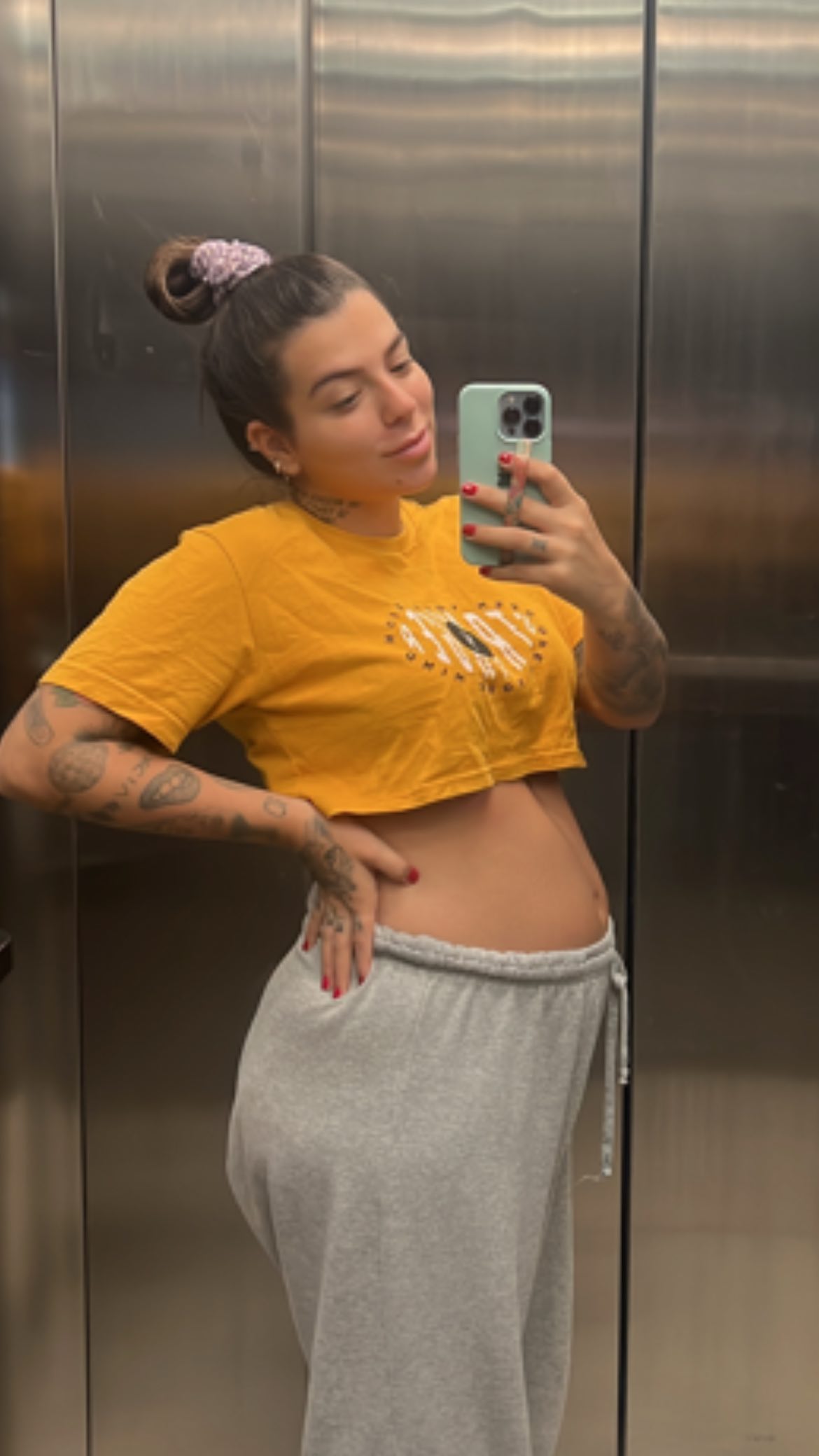 Petra Mattar posa em frente a um espelho usando apenas um cropped amarelo, enquanto deixa o barrigão de grávida aparecer