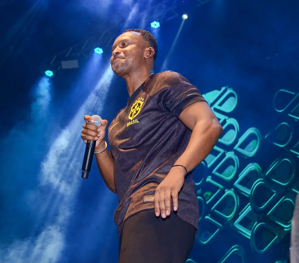 Thiaguinho cantando no palco enquanto usa uma camiseta preta da Seleção Brasileira