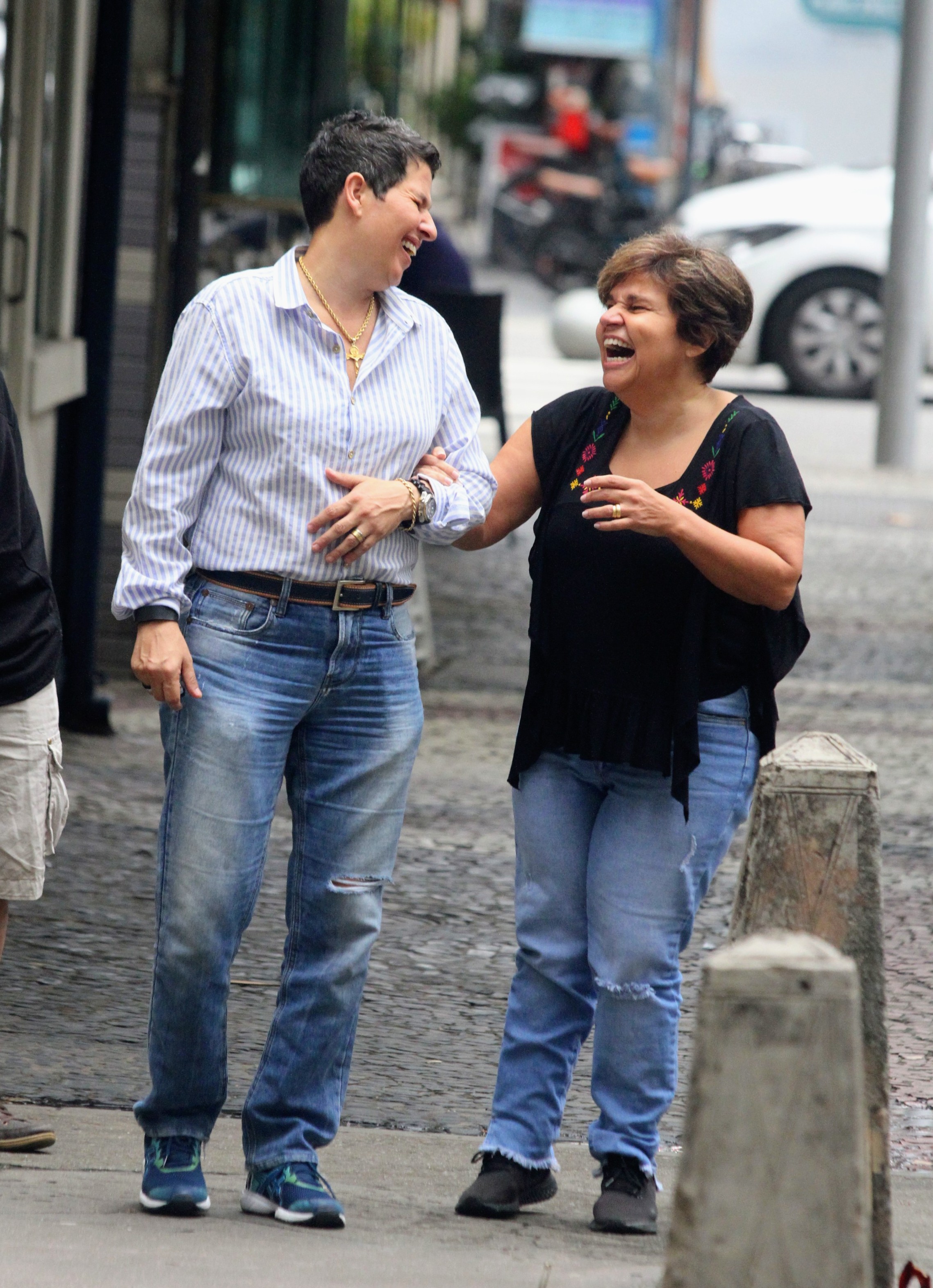 Foto de Adriane Bonato de braço dado com Claudia Rodrigues, ambas rindo muito enquanto caminham pela rua