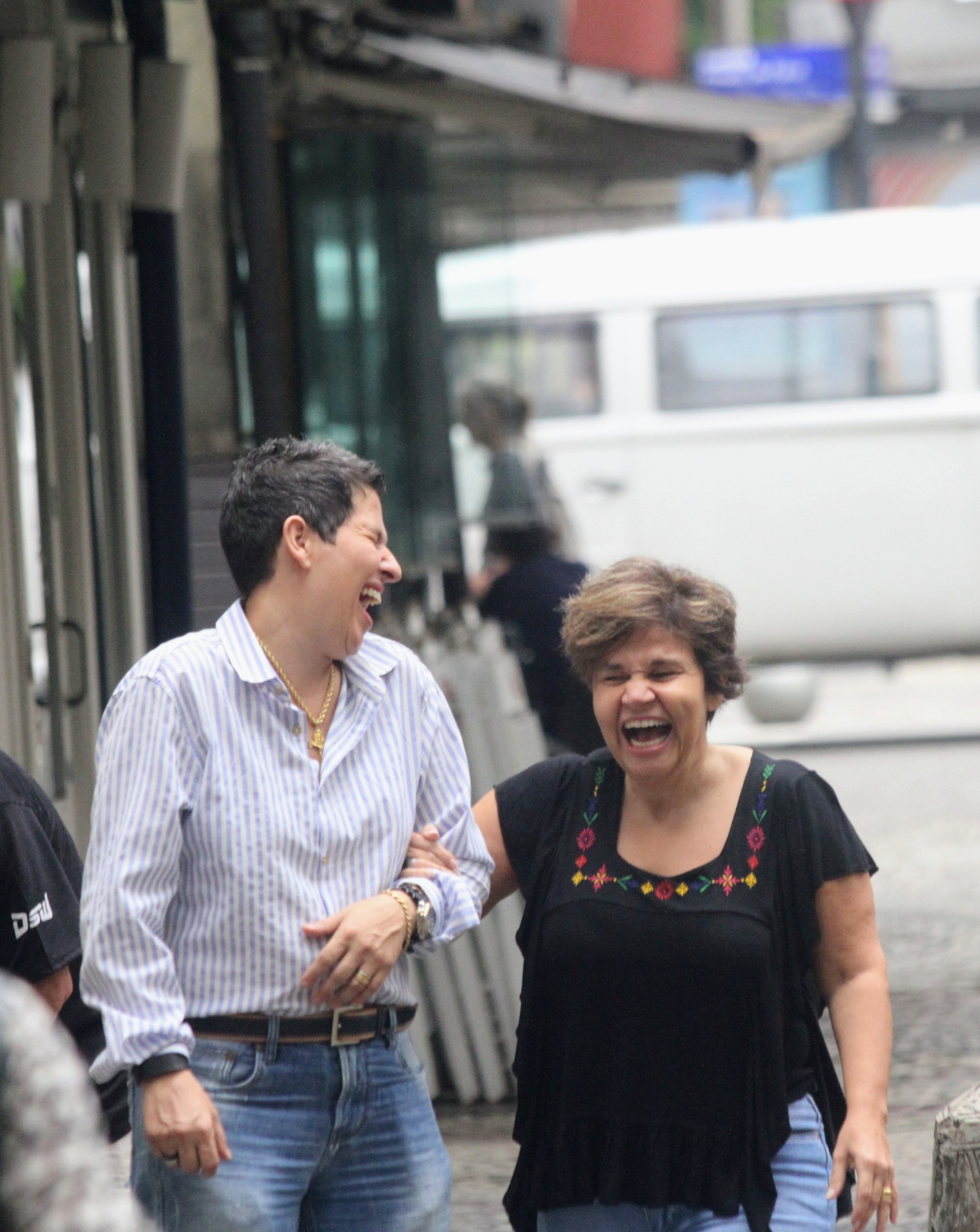 Foto de Adriane Bonato de braço dado com Claudia Rodrigues, ambas rindo muito enquanto caminham pela rua