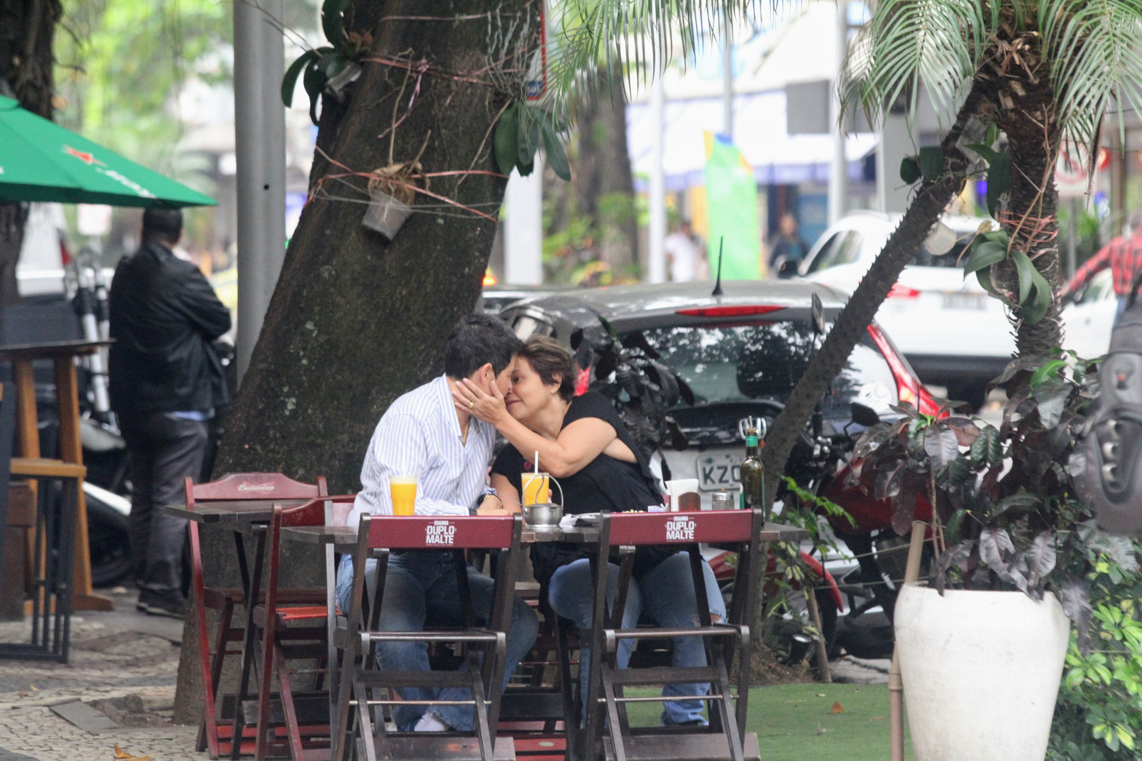 Foto de Adriane Bonato de braço dado com Claudia Rodrigues sentadas em uma mesa de bar trocando carinhos enquanto almoçam
