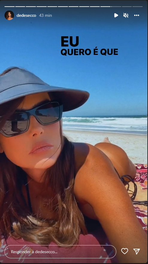 Foto retirada dos Stories de Deborah Secco em que ela aparece de bruços de biquíni, chapéu e óculos escuros na praia