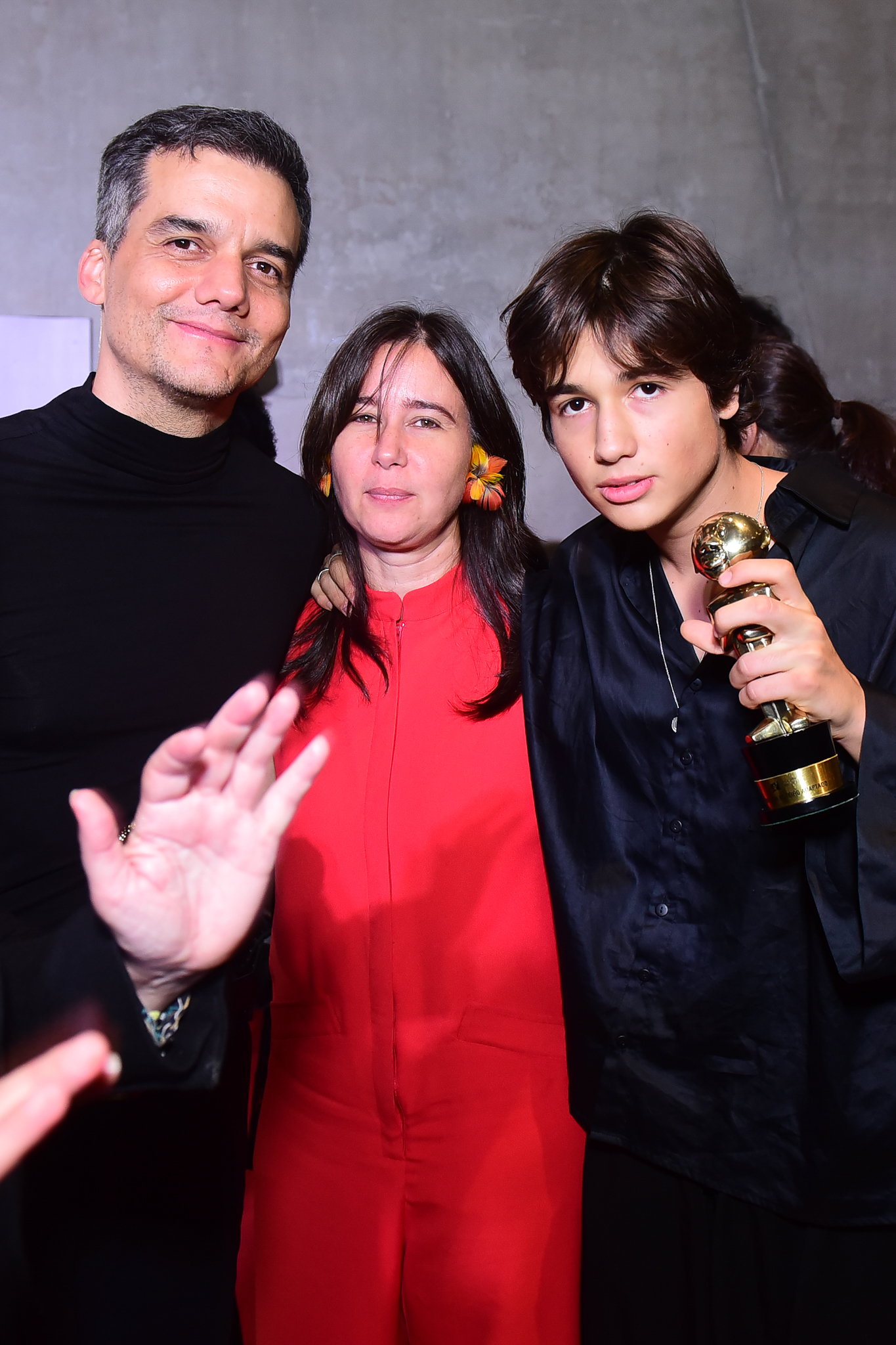 Foto de Wagner Moura, da esposa Sandra Delgado e do filho mais velho deles, Bem. Pai e filho seguram prêmios em um tapete vermelho