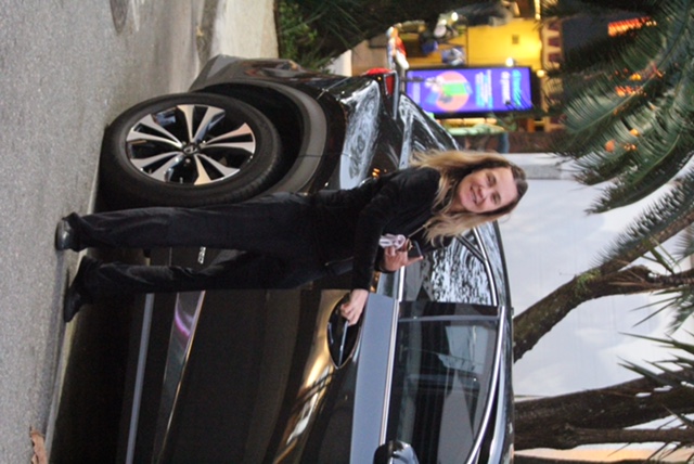 Foto da atriz Adriana Esteves entrando em um carro enquanto sorri para a câmera