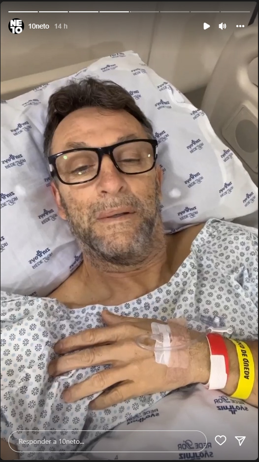 Craque Neto deitado em uma cama de hospital recebendo soro, de óculos e avental