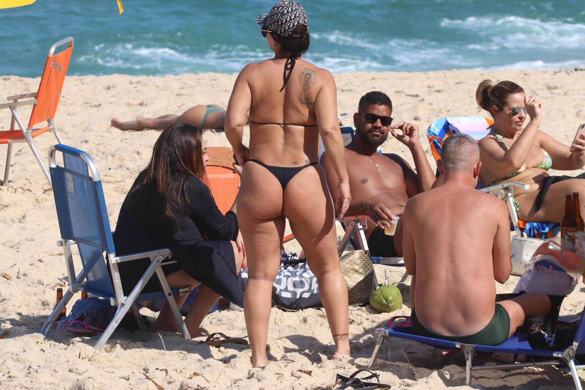 Foto de Viviane Araújo em pé, de costas, de biquíni, próxima a amigos em uma praia